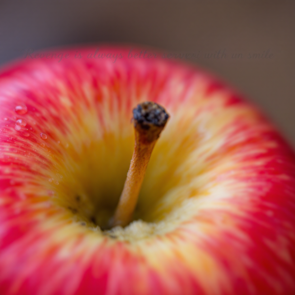 A close-up of a vibrant red apple, its surface glistening with moisture, symbolizes the quote, Revenge is always better served with a smile, suggesting a hidden sweetness.