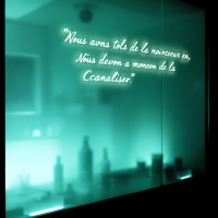 A softly lit room features a glowing quote in French about embracing and channeling inner darkness, surrounded by blurred silhouettes of bottles and objects.