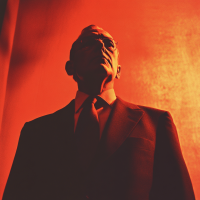 A stern man in a suit stands under dramatic red lighting, emphasizing his figurehead role, meant to captivate and distract rather than command power, as described in the book quote.