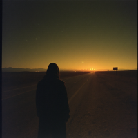 A lone figure stands on an empty road at sunset, silhouetted against a vibrant sky, embodying the mystery and depth of experiences unseen and losses unshared.