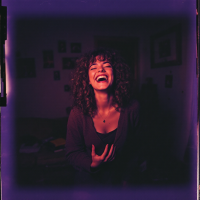 A woman with curly hair laughs joyfully, embodying the spirit of self-acceptance and humor, surrounded by a softly lit room filled with personal photos and memories.