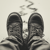 A close-up of black boots resting on the ground, with a wavy trail behind them, reflecting the quote about understanding others by walking in their shoes.